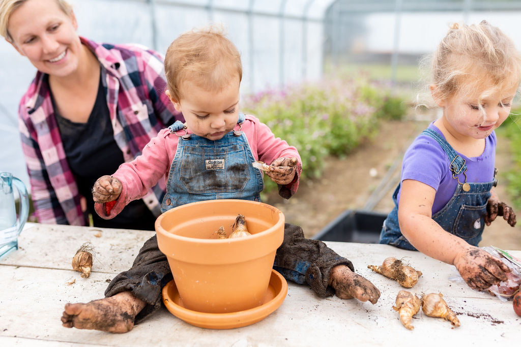 A caregiver and children planting in the Rooted Flowers greenhouse