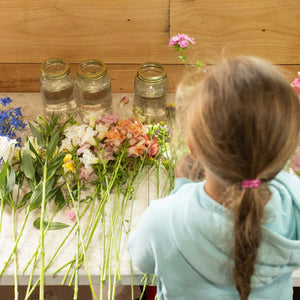 Child arranging flowers on a table with jars and a wooden wall background