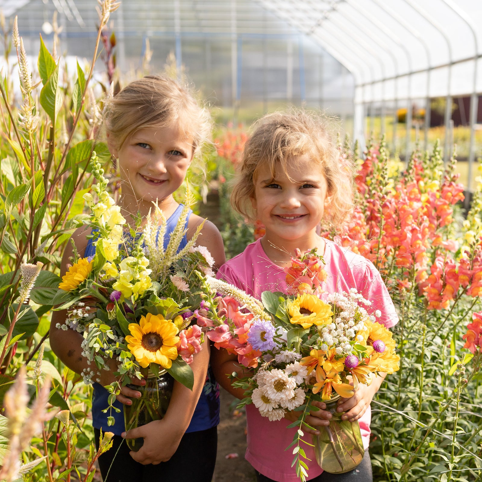 Two young girls holding flower bouquets in a greenhouse