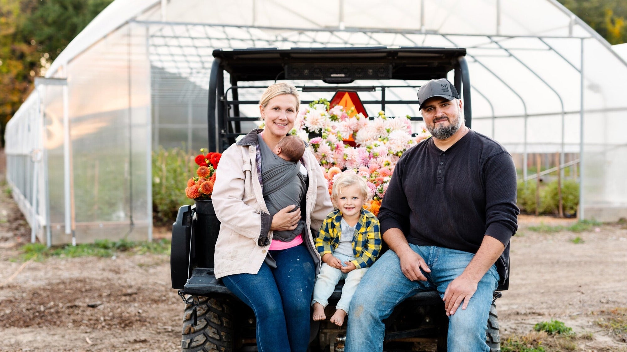 The Rooted Flowers family seated beside a cart full of flowers in front of a greenhouse.